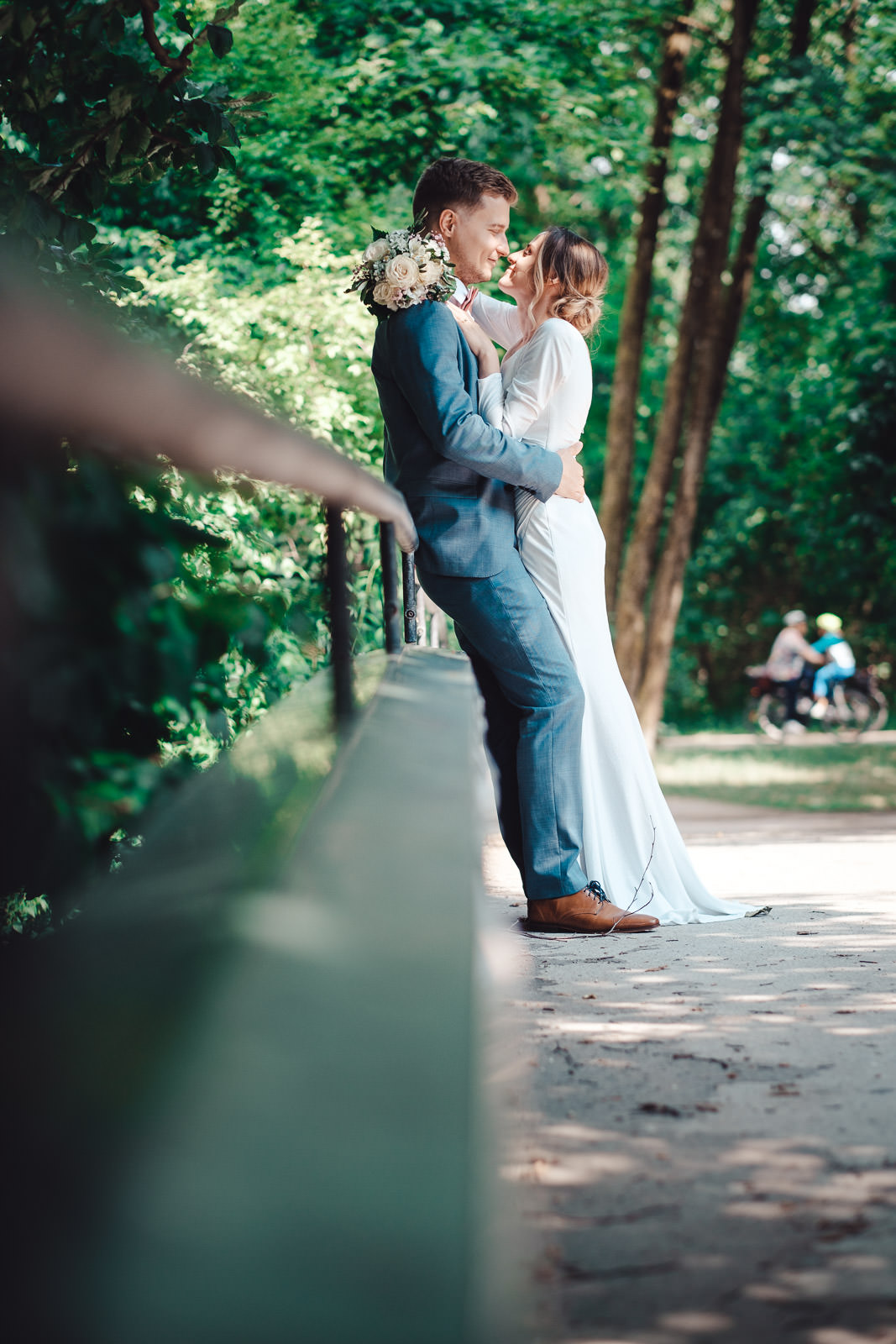 Hochzeitsfotograf München | Hochzeitsfotograf München Bride and groom share a kiss while embracing on a green park railing, bouquet in the groom's hand. - Hochzeitsfotograf München