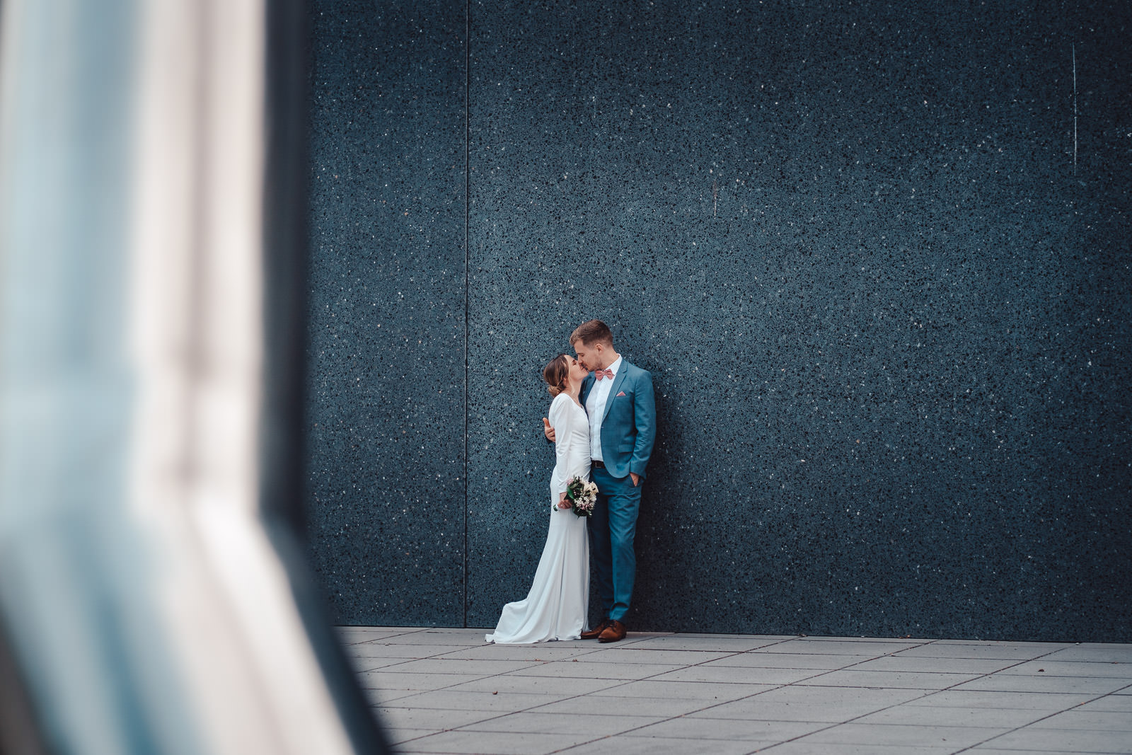 Hochzeitsfotograf München | Hochzeitsfotograf München Bride and groom sharing a kiss beside a dark speckled blue wall; she holds a bouquet. - Hochzeitsfotograf München