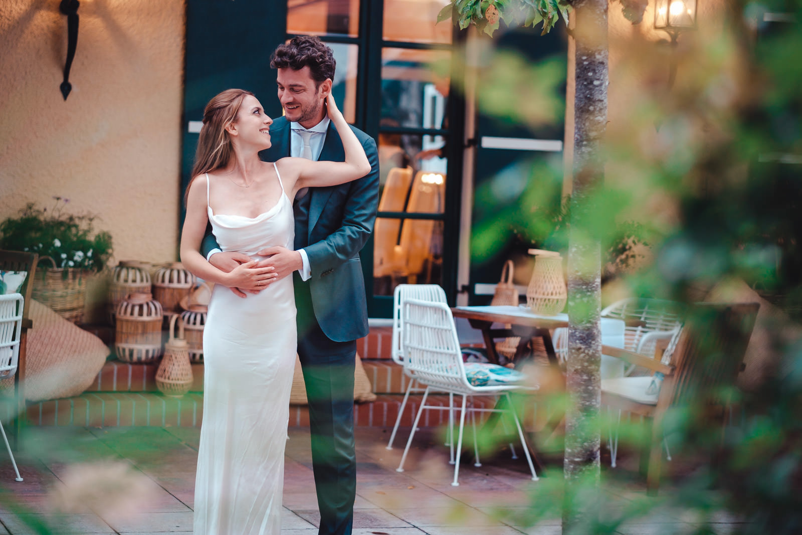 Hochzeitsfotograf München | Hochzeitsfotograf München A smiling couple embraces on an outdoor patio; woman in a white dress and man in a blue suit. - Hochzeitsfotograf München